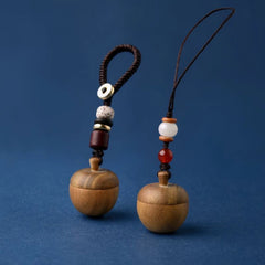 Two wooden apple keepsake urn keychains standing on a blue background, showing bead and strap details.