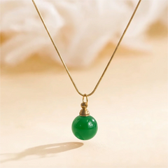 Green agate urn necklace photographed on warm beige background with natural sunlight, symbol of peace and renewal.