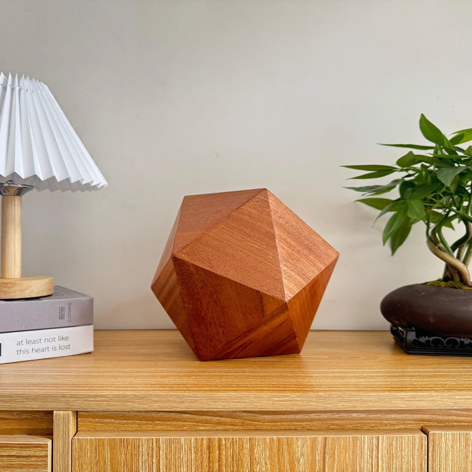 Lyra Pet Urn in sapele wood, icosahedron on tabletop, close-up grain detail.