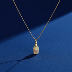 Ocean chalcedony agate pendant necklace on a gold chain, photographed on a deep blue background with soft natural light and shadow.