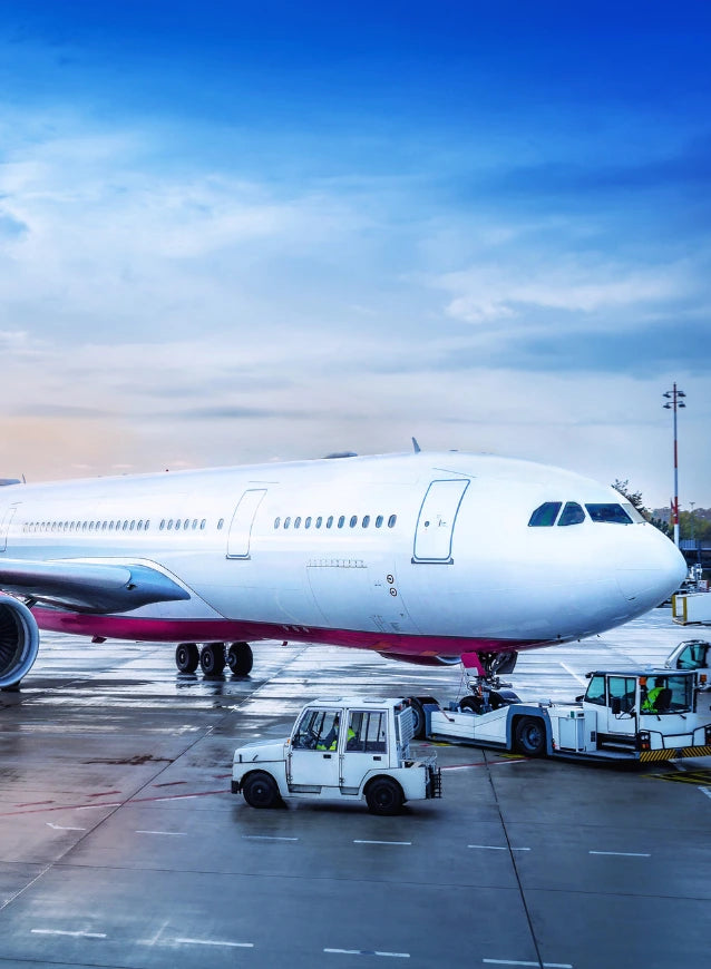 Airplane at an airport with ground crew and tug, representing worldwide shipping.