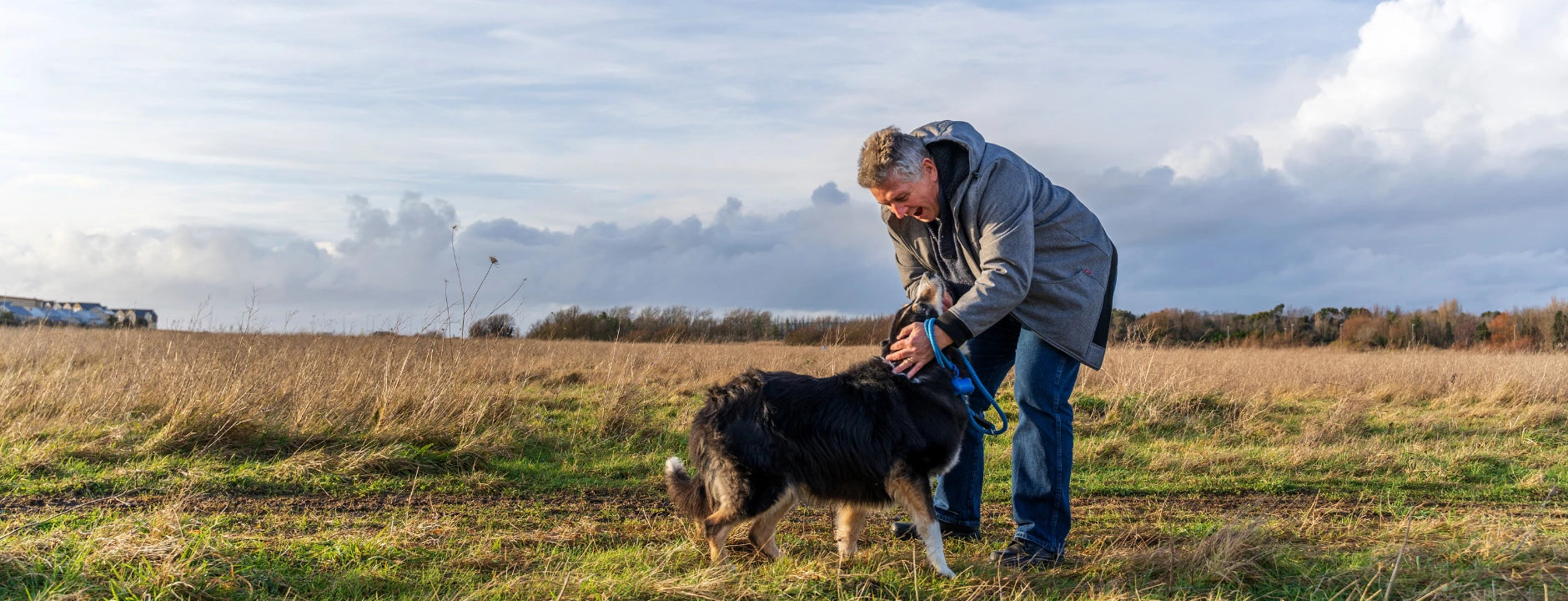 Wide Contact Us banner of a man bending to pet his dog in an open field.