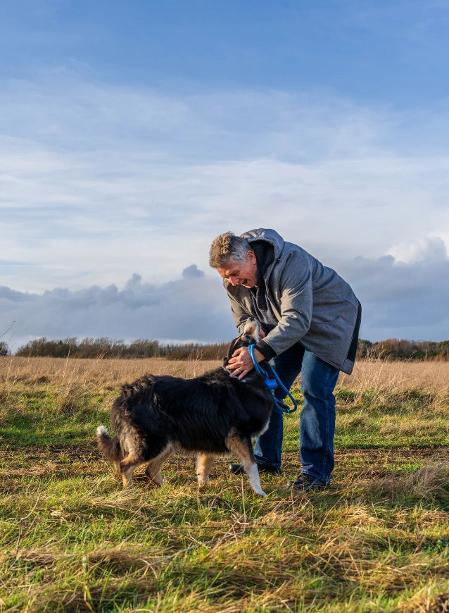 Contact Us banner: man petting a dog in a grassy field under a cloudy